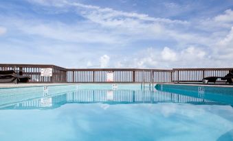 a large swimming pool with a wooden fence surrounding it , reflecting the blue sky and clouds above at Lime Tree Bay Resort