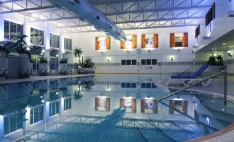 an indoor swimming pool with a water slide , surrounded by buildings and lit up at night at Village Hotel Birmingham Dudley