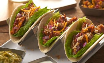 three tacos on a metal tray with various side dishes and a glass of water in the background at Hyatt Place Saratoga Malta