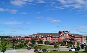 a large hotel with a red and green sign is surrounded by a parking lot and trees at Norfolk Lodge & Suites, Ascend Hotel Collection