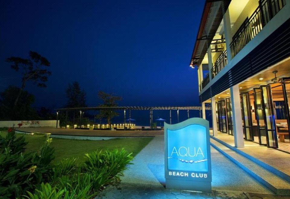 There is a sign for the beach at night, with an apartment complex located behind it at Holiday Palace Casino Resort Sihanoukville