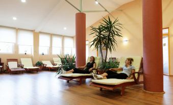 two women are relaxing on lounge chairs in a room with wooden floors , surrounded by potted plants at Hotel Perla