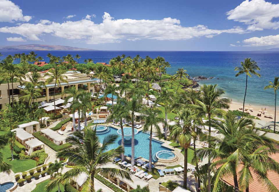a resort with a large pool surrounded by palm trees , and the ocean in the background at Four Seasons Resort Maui at Wailea