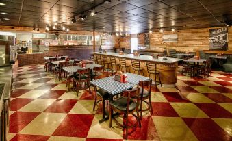 a large , well - lit restaurant with wooden walls and red and white checkered flooring , containing multiple dining tables and chairs arranged around the space at LaJunta Inn