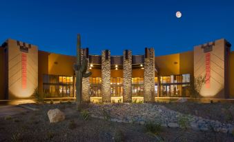 a large , modern building with stone and wood exterior is lit up at night , surrounded by trees and cacti at Desert Diamond Casino