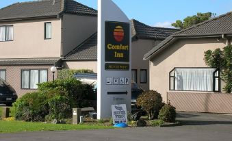 a large sign for the comfort inn is displayed in front of a house , with a car parked nearby at Auckland Airport Motel