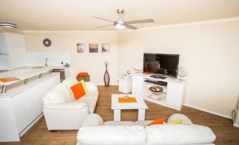 a living room with a white couch , orange pillows , and a flat - screen tv mounted on the wall at Sanctuary Beach Resort