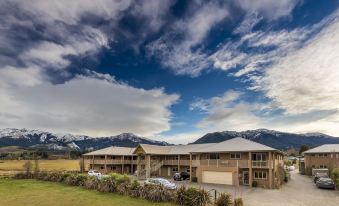 a large building with a blue sky and mountains in the background , and cars parked on the street at Hanmer Springs Retreat