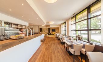 a modern restaurant with wooden flooring , large windows , and multiple dining tables set for guests at Select Hotel Erlangen