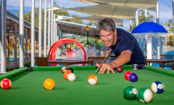 a man is playing pool , surrounded by various colored balls on a green pool table at Ingenia Holidays Lake Conjola