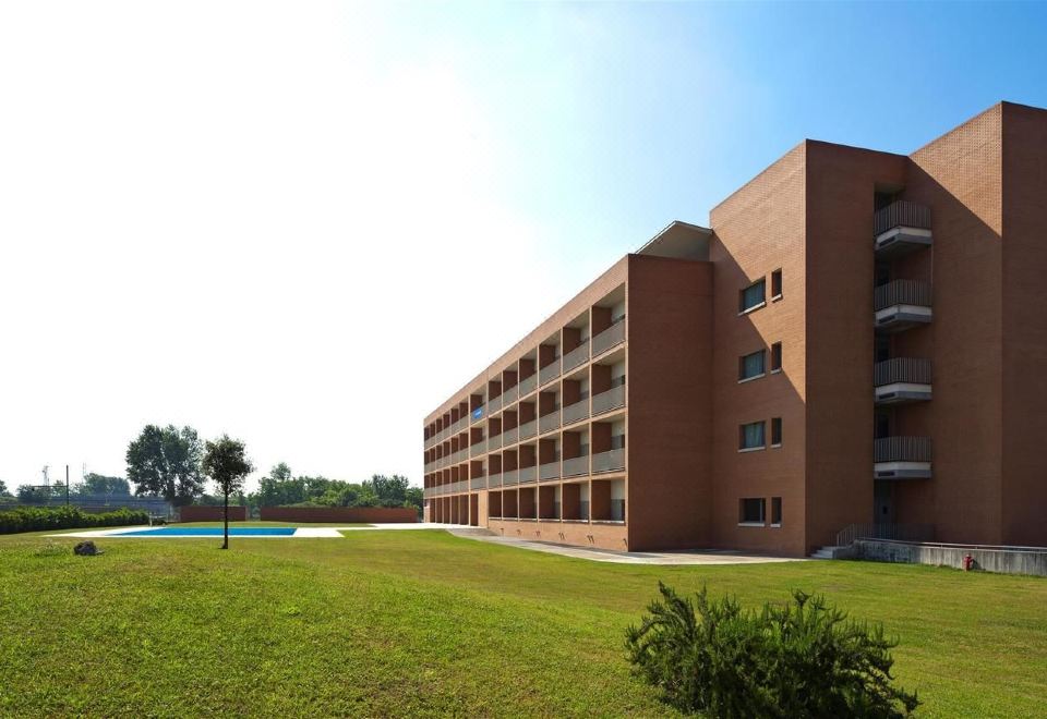 a large brick building with multiple floors and balconies , situated on a grassy field near a swimming pool at Inn Naples Airport