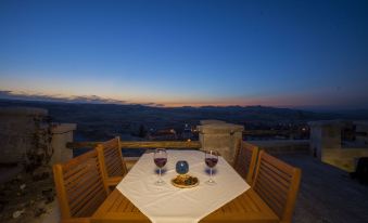 a wooden table with two wine glasses and a bowl of cheese is set up on a patio overlooking the city at Azure Cave Suites - Cappadocia