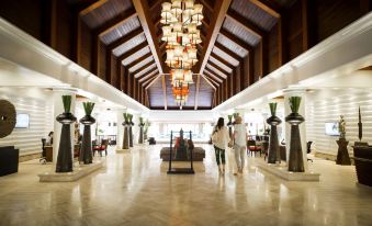 a large hotel lobby with wooden pillars , a grand chandelier hanging from the ceiling , and several people standing near the reception desk at Robinson Khao Lak