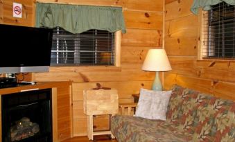 a cozy living room with wooden walls , a fireplace , and a couch in front of a window at Linville River Log Cabins
