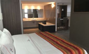a modern bedroom with a large bed , striped bedspread , and a modern kitchen in the background at Hangar Inn Guadalajara Aeropuerto