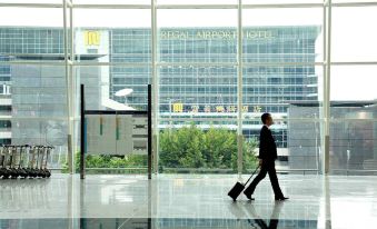 A man walks through an airport with his luggage towards the entrance of a different large building at Regal Airport Hotel