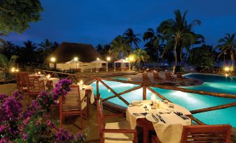a beautiful outdoor dining area at a resort , with tables and chairs set up for guests to enjoy their meals at Diamonds Malindi