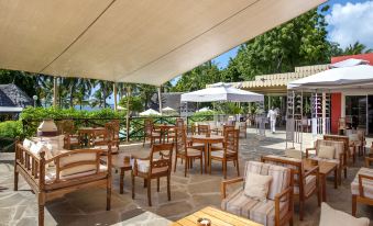 a patio area with wooden furniture , umbrellas , and people sitting at tables under a large white tent at Diamonds Malindi