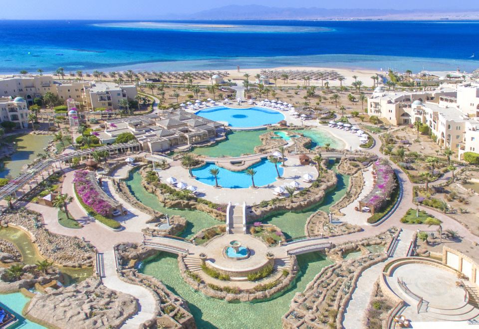 aerial view of a resort with a large pool surrounded by palm trees , beach chairs , and umbrellas at Kempinski Hotel Soma Bay