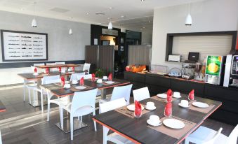 a modern restaurant with white chairs and tables , red napkins , and a bar area in the background at Adonis Paris Sud