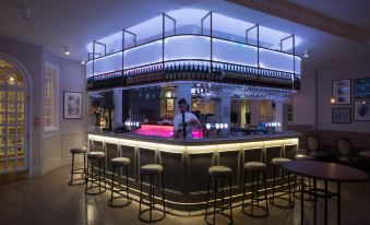 a well - lit bar with a blue and purple color scheme , multiple stools , and a bartender at the counter at The Kings Head Hotel