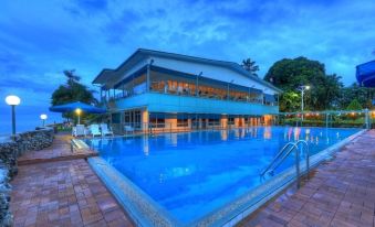a large swimming pool with a building in the background and palm trees surrounding it at Madang Resort