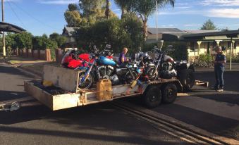 a group of people are riding on a trailer carrying several motorcycles and atvs , set against a sunny backdrop at Oasis Motel