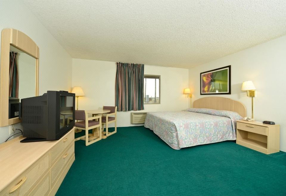 a hotel room with a green carpet , wooden bed , desk , chair , and television on the wall at Americas Best Value Inn Eloy/Casa Grande