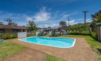 a backyard with a pool surrounded by grass , chairs , and umbrellas , as well as a house in the background at Lemon Tree Passage Motel