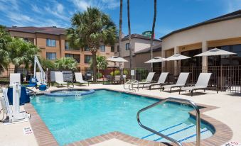 a beautiful swimming pool area with sun loungers , umbrellas , and palm trees in front of a hotel at Courtyard Harlingen