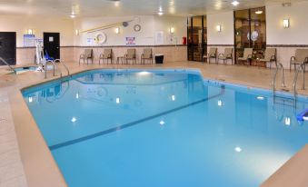 an empty indoor swimming pool with clear blue water , surrounded by chairs and tables , in a well - lit room at Ramada Plaza by Wyndham Sheridan Hotel & Convention Center