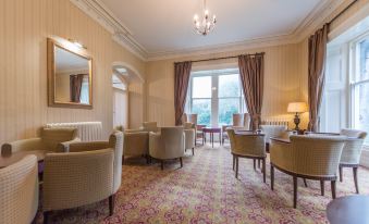 a spacious living room with comfortable seating , a chandelier , and large windows that offer views of the city at Cumbria Grand Hotel