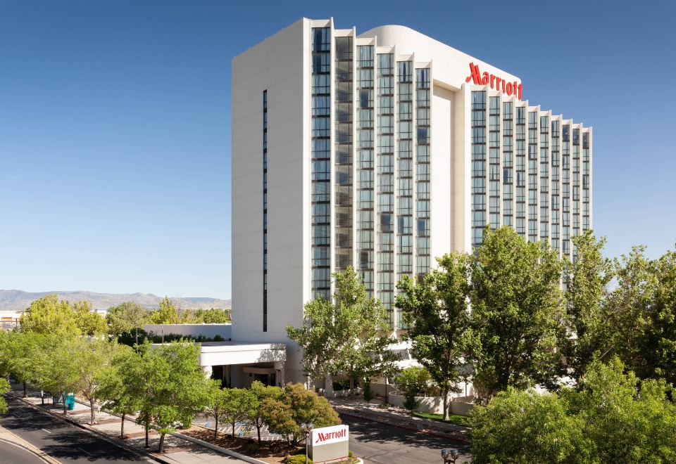 a large hotel with a red sign on top is surrounded by trees and cars at Marriott Albuquerque