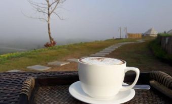 a cup of coffee sits on a table with a view of a tree and a house in the background at Chiangkhan River Green Hill