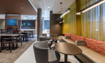 a modern lounge area with gray and orange seating , wooden tables , and yellow walls , under a ceiling with hanging lights at SpringHill Suites Columbia