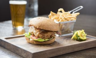 a wooden dining table with a plate of food , including a burger , fries , and a beer at McKinley Chalet Resort