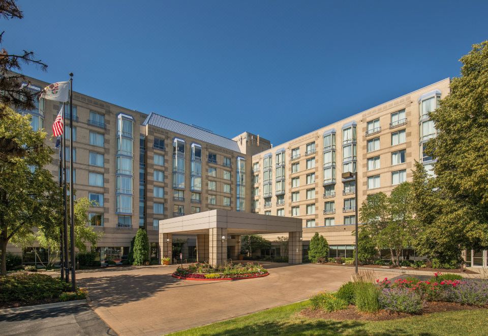 a large hotel with a parking lot in front of it , surrounded by trees and bushes at Sheraton Suites Chicago Elk Grove