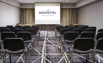 a conference room with rows of black chairs and a large screen displaying the logo for novotel hotel & apartments at Novotel Manchester West