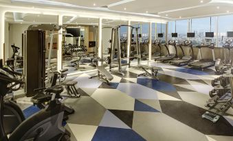 a well - equipped gym with various exercise equipment , including treadmills and weightlifting machines , positioned in a spacious room with large windows at Novotel Jakarta Mangga Dua Square