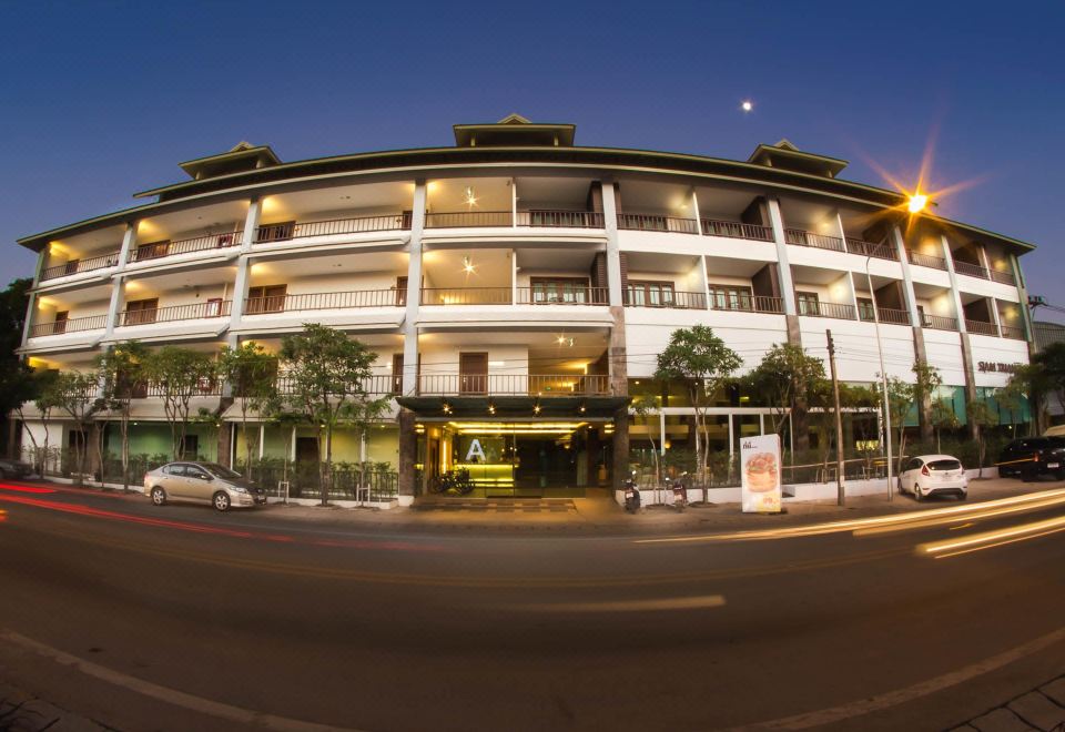 a modern building with multiple floors , surrounded by trees and cars on the street at night at Siam Triangle Hotel