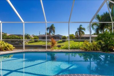 a swimming pool surrounded by a patio , with a view of palm trees and a house in the background at Italy