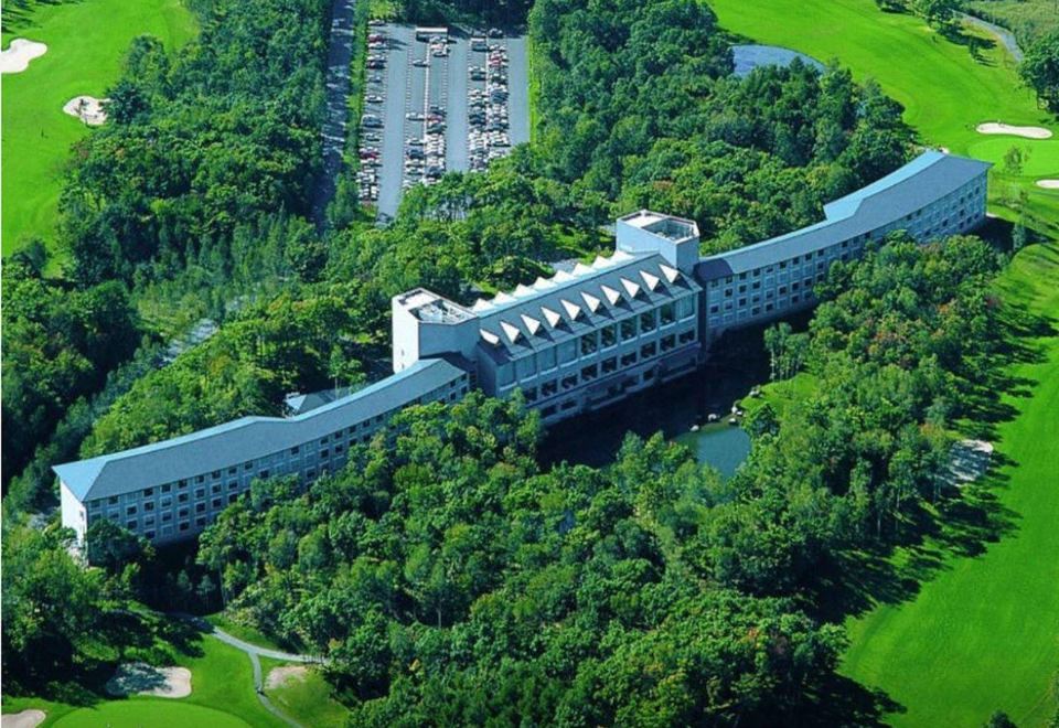 an aerial view of a large building surrounded by trees , with a parking lot in the foreground at Hakodate-Onuma Prince Hotel