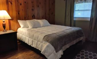 a large bed with white sheets and a gray blanket is in a room with wooden walls at RiverBend Lodge