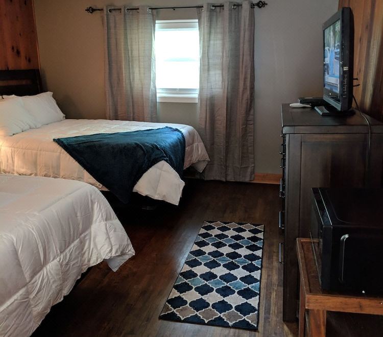 a cozy bedroom with two beds , a window , and a tv , all neatly arranged on a wooden floor at RiverBend Lodge