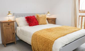 a white bed with a yellow blanket and red pillow is in a room with two nightstands at The Cow Shed