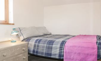 a bed with a blue and white plaid comforter , a pink blanket , and a lamp on a nightstand at The Cow Shed