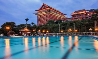 At night, there is a large building with a pool in front and a hotel behind it at The Grand Hotel