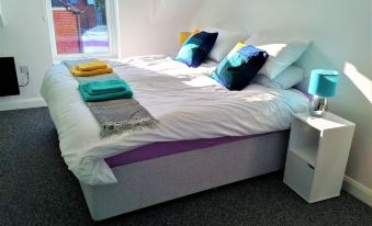 a white bed with two blue and yellow pillows , a white headboard , and matching sheets at The Nest