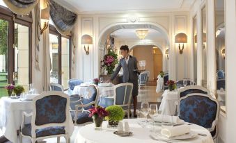 a man in a suit is standing at a table in a restaurant with white chairs and blue tablecloths at Auberge du Jeu de Paume