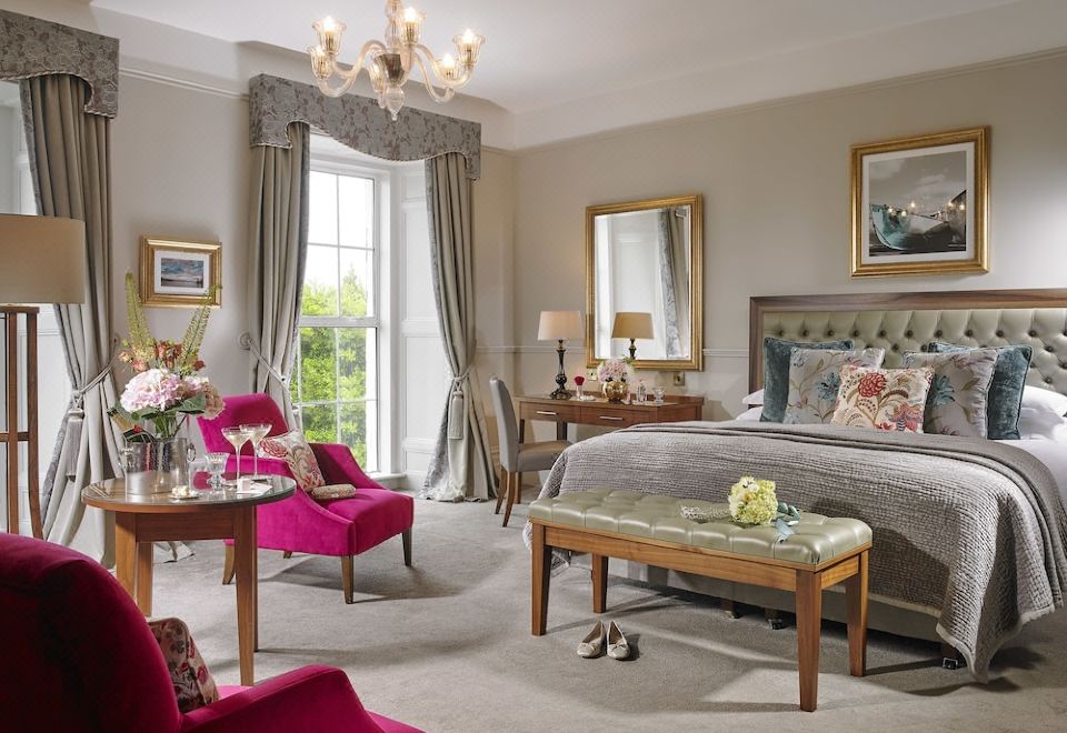 a luxurious bedroom with a large bed , pink chairs , and a chandelier , decorated with elegant furniture and greenery at Actons Hotel Kinsale